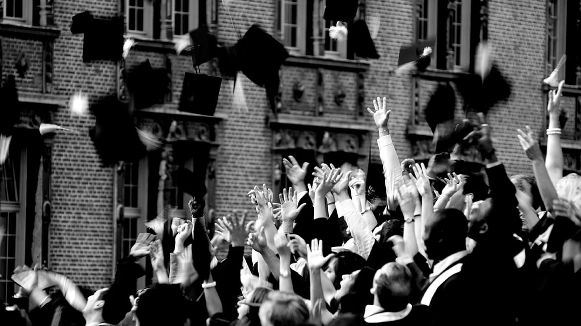 Black and white photo of group throwing graduation caps in the air.