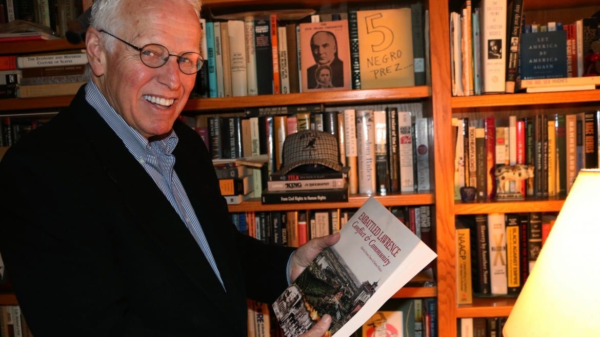 Photo of man holding book in front of bookcase.