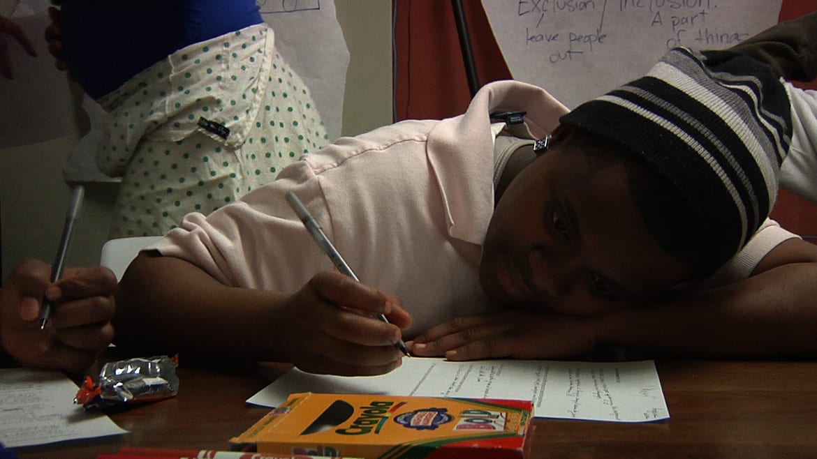 Image of young woman sitting with head down on a desk as she fills out a worksheet.