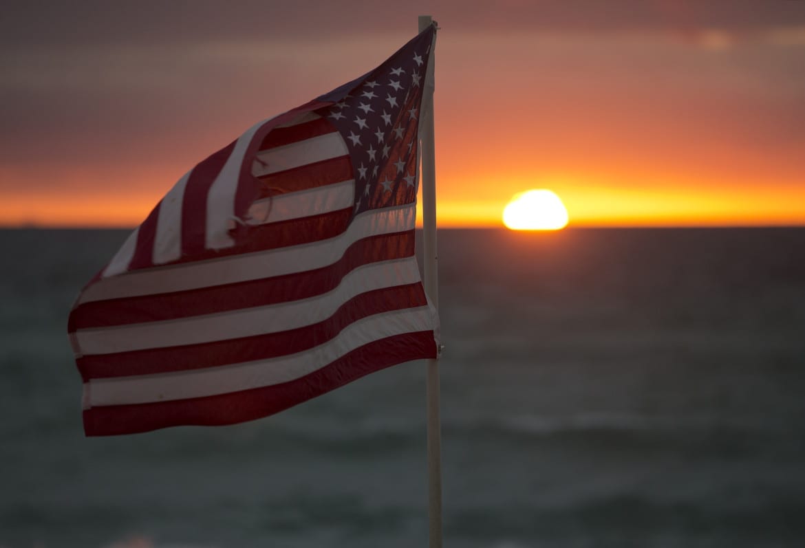 The flag of the United States is set against a sunset.