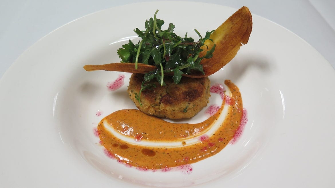 A crab cake with a chip and sauce.