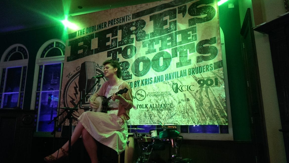 A woman sits with her guitar.
