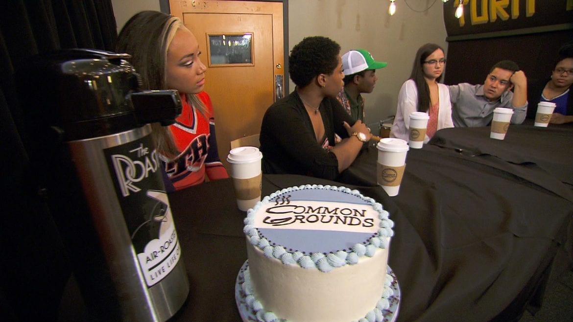 Teens sit at a table with a cake and coffee.