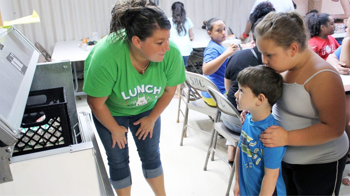 Kristen Hanks, who works in the Fort Osage school district cafeteria program, hands out lunches at Susquehanna Baptist Church in Independence, Missouri, a government-funded summer meal site. For children in the Kansas City metro area, food insecurity rises in the summer, but food sites like these are rare in rural areas. (Lindsay Huth | Flatland