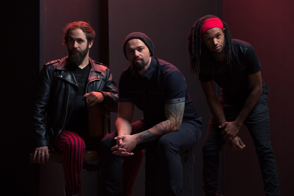 Three men in a band sit in a dark room.