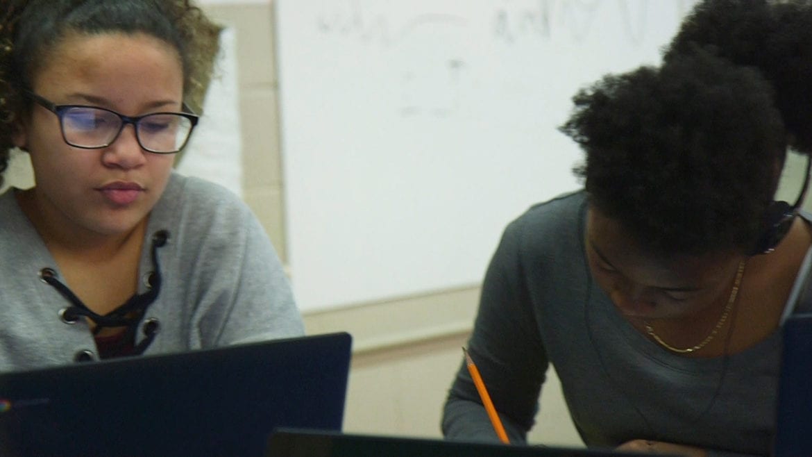 two young women at work, one on computer, one with a pencil
