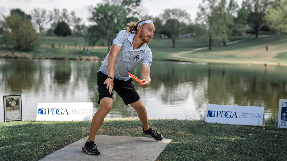 A disc golfer tees off from across a lake.