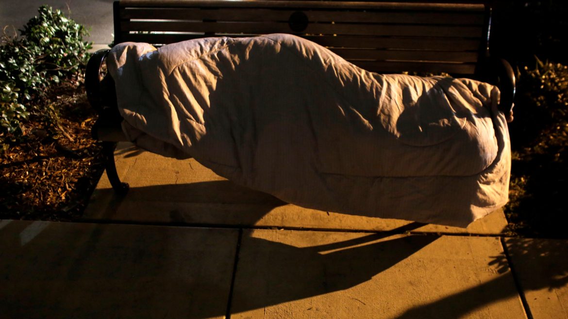 A homeless person sleeps on a bench as volunteers and homeless outreach officials walk in the area during the Point In Time Homeless Census in Miami.