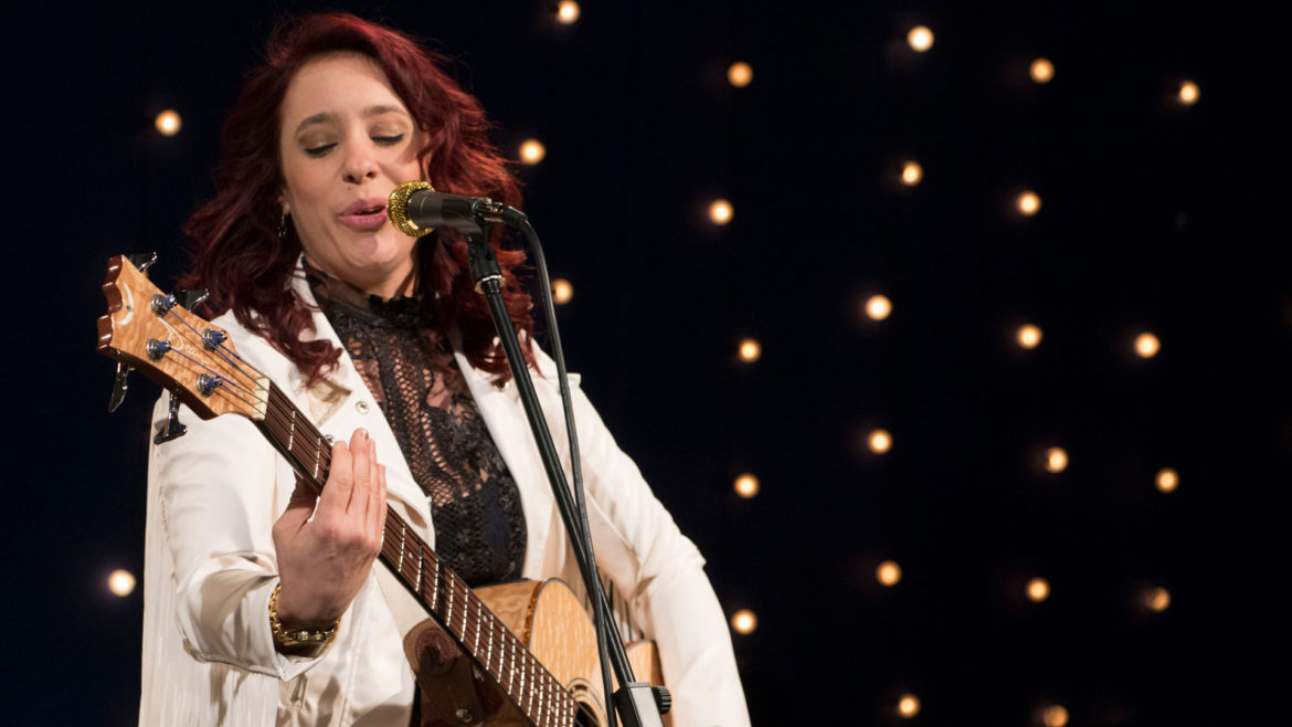 Danielle Nicole plays the guitar and sings into a mic.