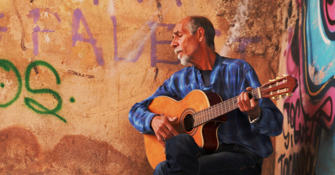 Man playing guitar on a stool