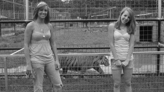 Karr and her sister pose infront of a pacing tiger in a cage.