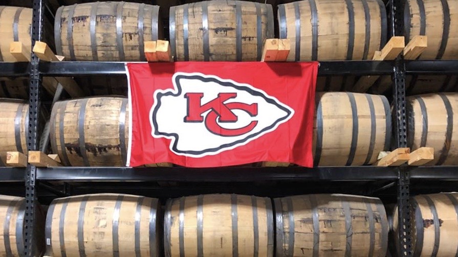 A Chiefs flag hangs on barrels of whiskey at J. Rieger & Co. Distillery