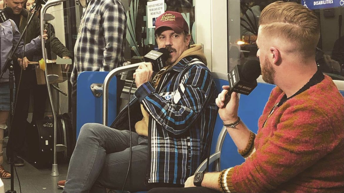Jason Sudeikis speaks into a microphone aboard the KC streetcar.