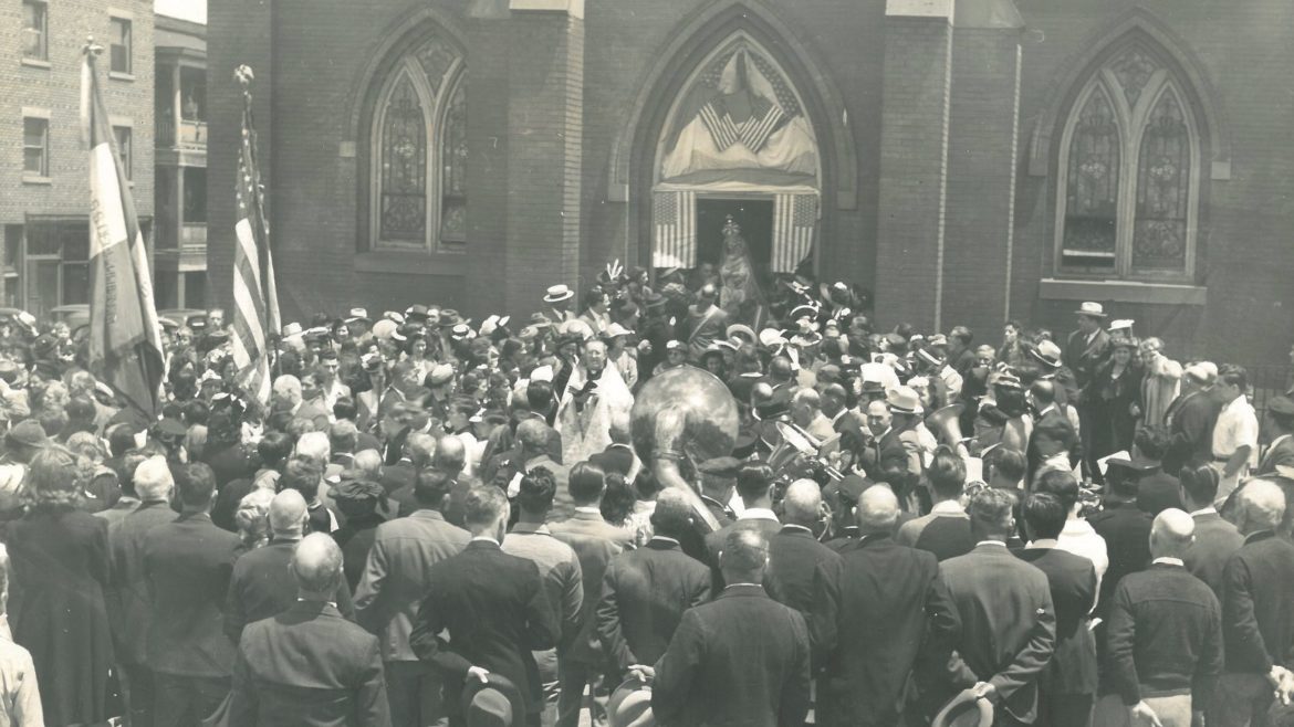 A crowd gathers around a priest outside of Holy Rosary Church.