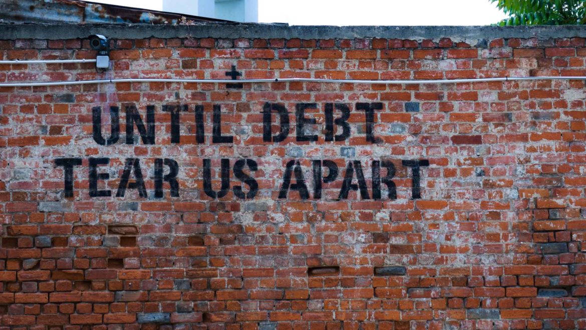 A brick wall painted with the words "Until Debt Tear Us Apart."