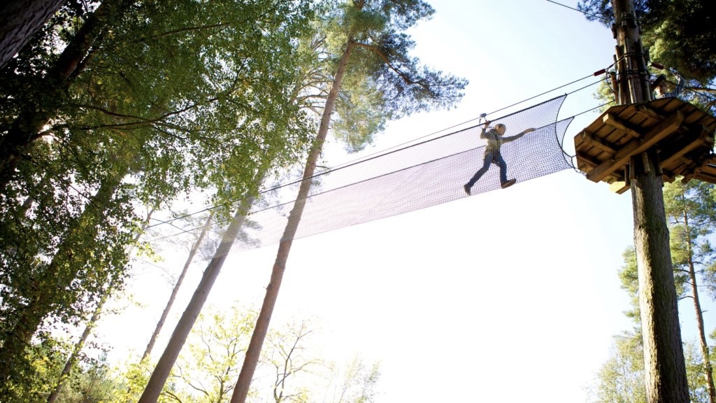 A person climbs across a rope bridge in treetops.
