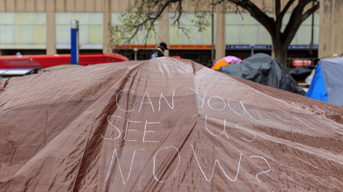 A hand drawn sign appears on a tarp covering tents at the Kansas City Homeless Union’s City Hall occupation on April 7.