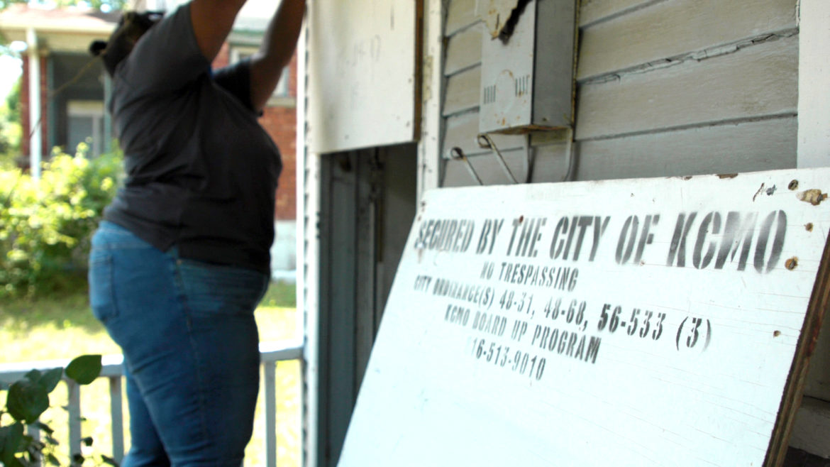 code enforcement officer DeJuan Carpenter removes screws from the piece of wood blocking entry to 2404 Monroe Ave., a vacant home in the Land Bank Program. (Cody Boston | Flatland)