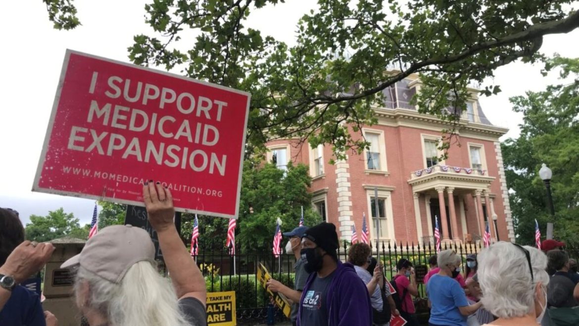 Demonstrators stand outside of the Governor’s Mansion in Jefferson City on July 1, 2021 and hold signs urging Gov. Mike Parson to fund voter-approved Medicaid expansion.