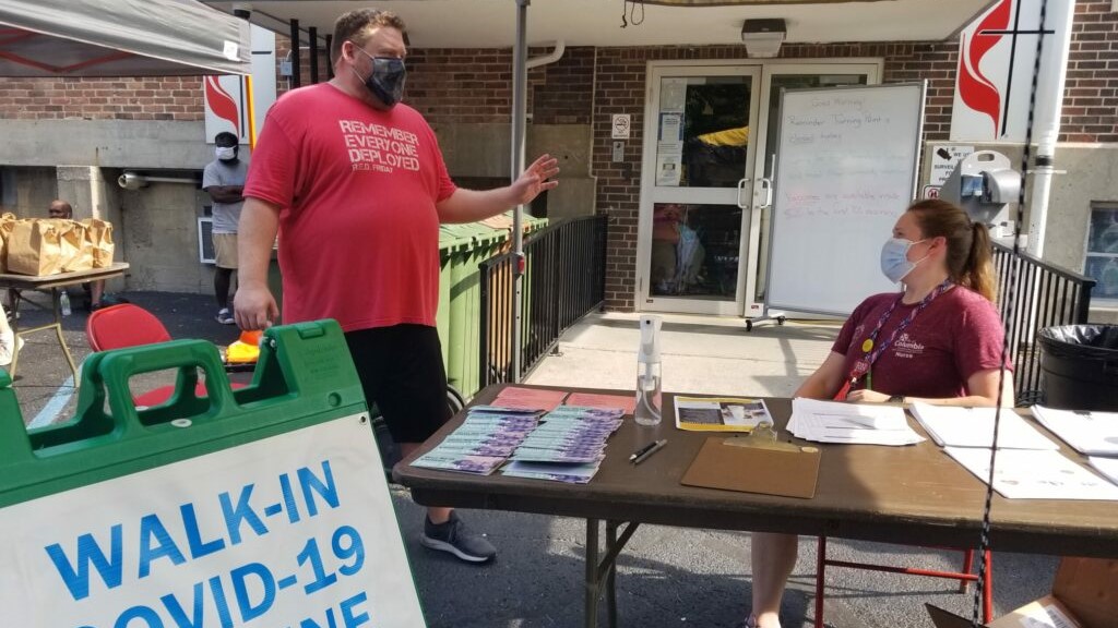 Mark Kirchhoff, left, a volunteer with Columbia Project Homeless Connect, speaks July 29, 2021 with Taylor Knoth, a public health nurse, at the registration table for a COVID-19 vaccination clinic.