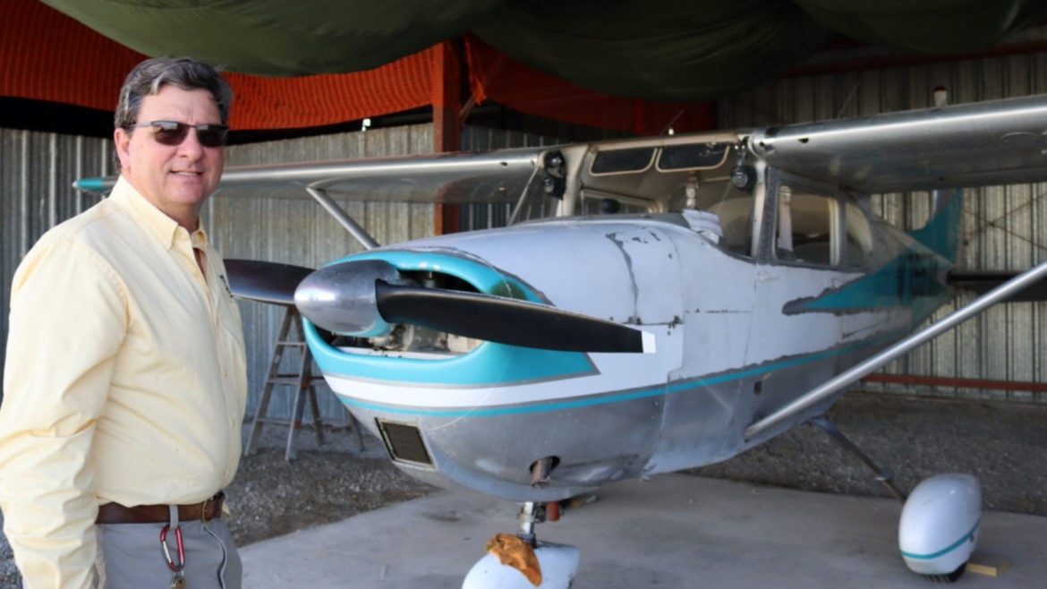Man smiles in front of a small vintage propeller plane.