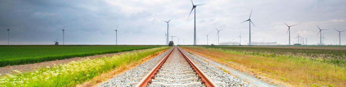 Train tracks against a backdrop of green grass and wind turbines illustrates a new project called the Grain Belt Express. This new effort is a "massive high-powered transmission line delivering renewable energy."
