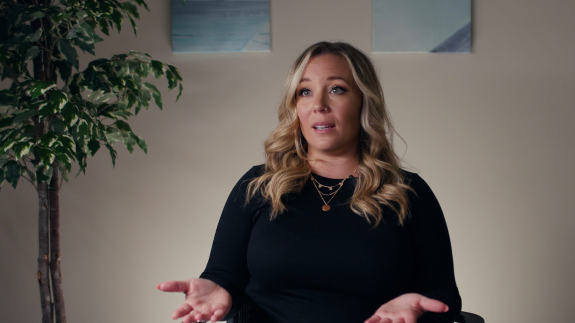 woman with blonde hair and plant in the background.