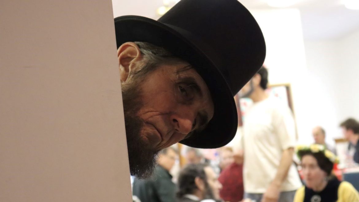 A man dressed as Abraham Lincoln peaks around a wall.