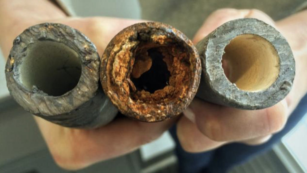 An individual holds a lead pipe, a steel pipe and a lead pipe treated with protective orthophosphate.