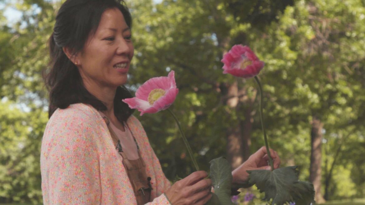 A woman holds two tall-stemmed pink flowers and smiles.