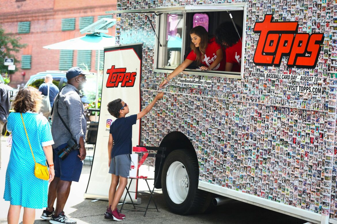 A boy is handed trading cards from a Topps Truck decorated with baseball cards.