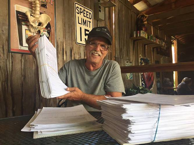 man with hat and glasses holds up papers.