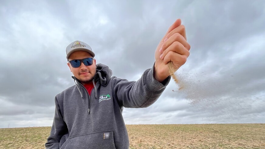 Farmer Alex Millershaski watches the wind blow a handful of dry, sandy soil across one of his wheat fields. His county in southwest Kansas just experienced its driest October on record.