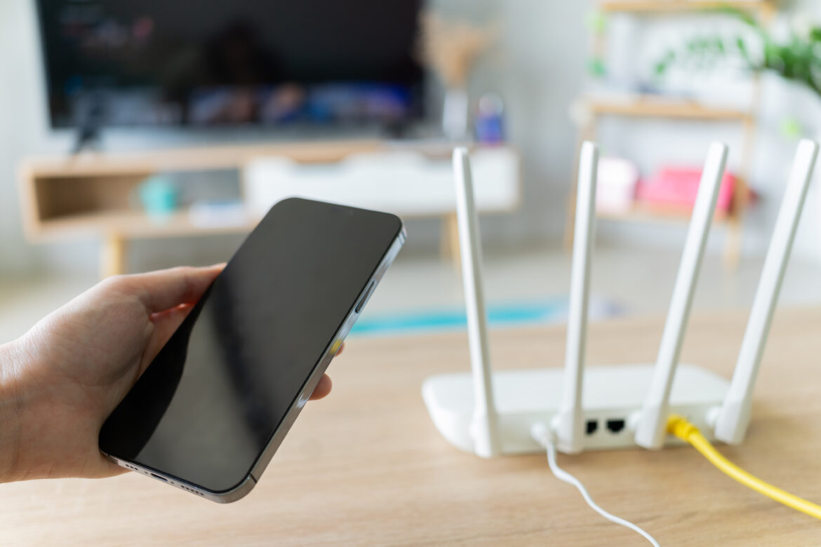 Wi-Fi router sits on a table while someone holds a smartphone.