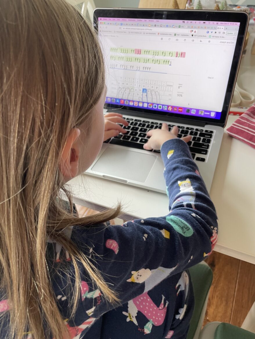 Young girl sits at a laptop practicing her typing skills.