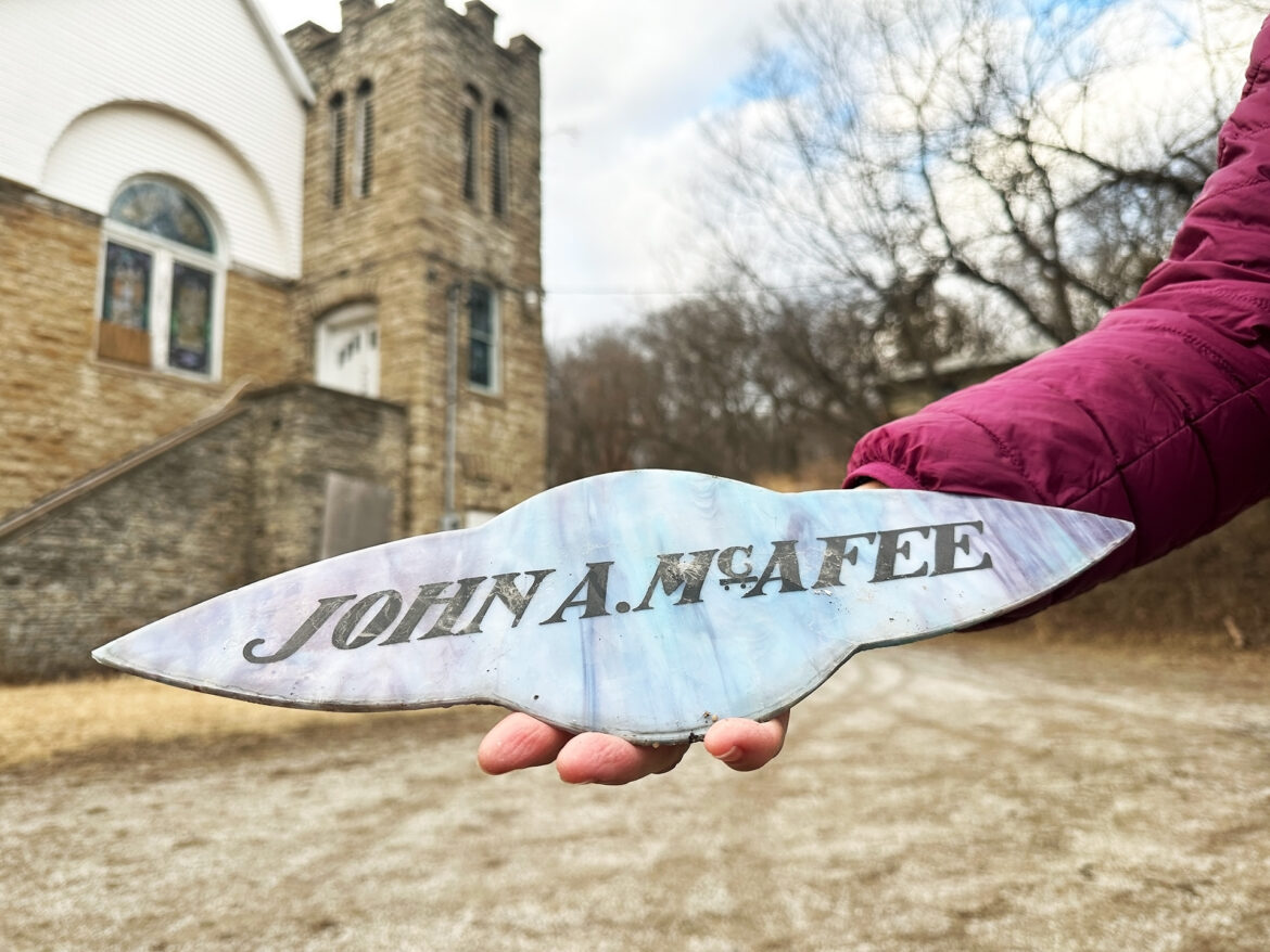 Hand holding a piece of stained glass window with the name John A McAfee on it.