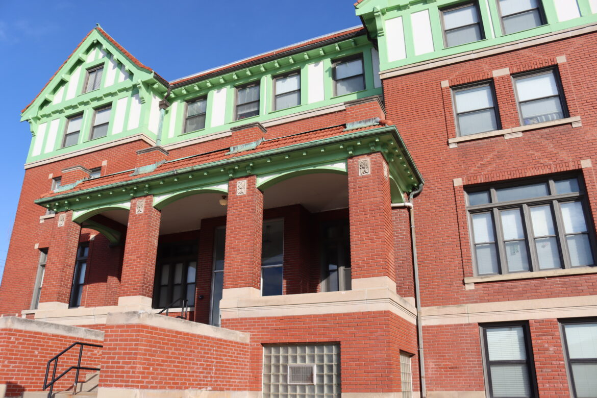 A brick building with Tudor styling and green trim on top.