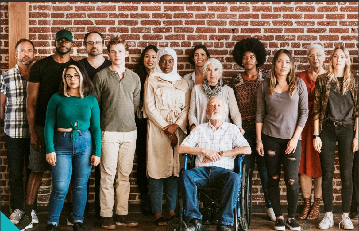 Fourteen people posing in front of a brick wall.