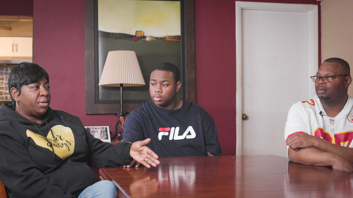 The Mitchell family sits around their kitchen table. Michelle is seated next to 17-year-old son with autism, explaining what she faces juggling work and finding support for her son.