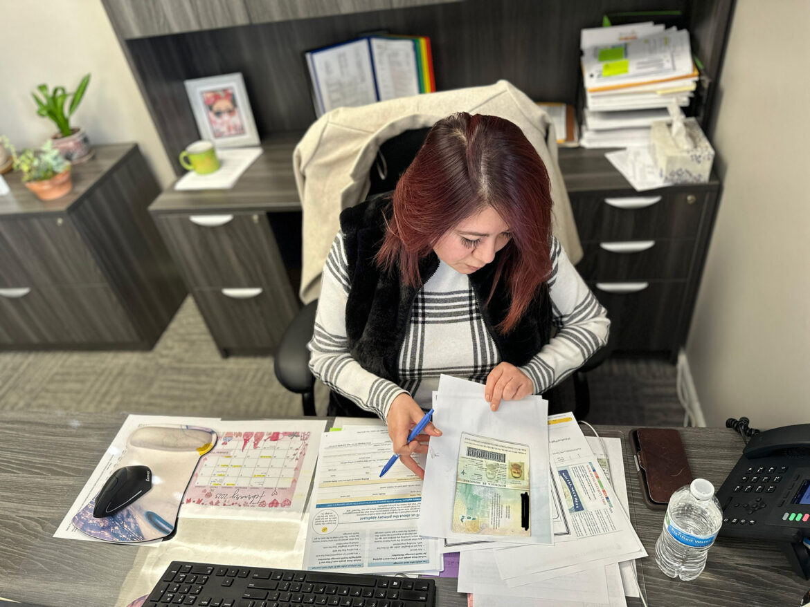 A woman with papers scattered around her on her desk. Ivonne Montanez is a health navigator at El Centro. Here she prepares one of her clients' Medicaid applications. (Vicky Diaz-Camacho | Flatland)