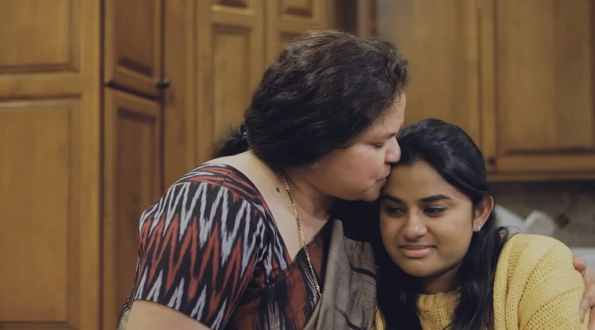 A mother kisses her daughter on the forehead. The daughter is crying,