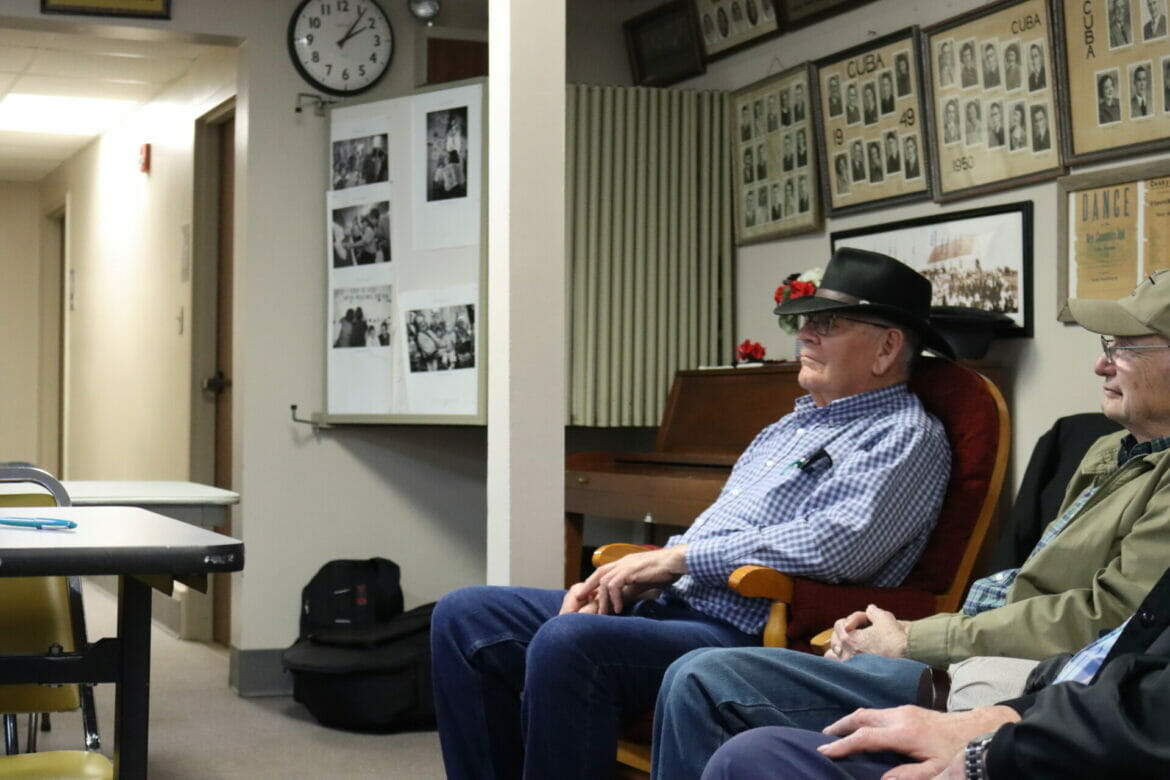 A man in a black cowboy hat sits in a rocking chair.