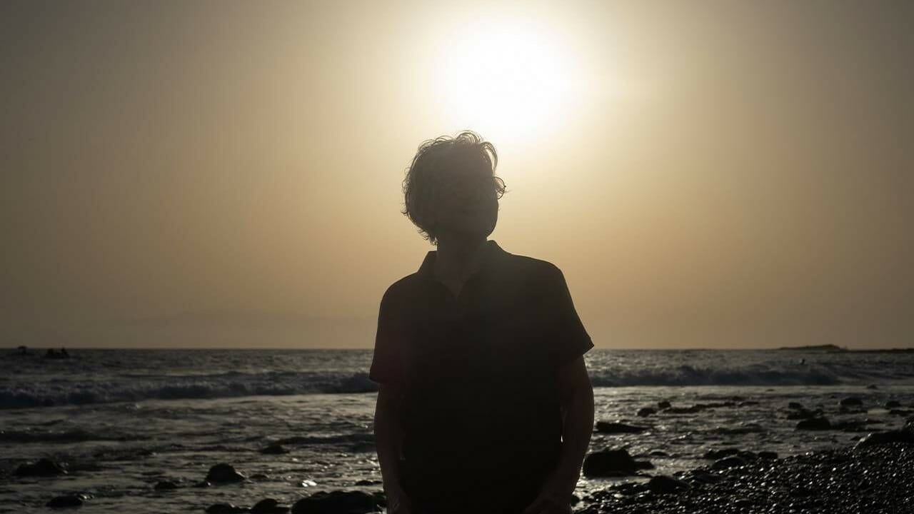 A woman walking on a beach with the sun setting behind her.