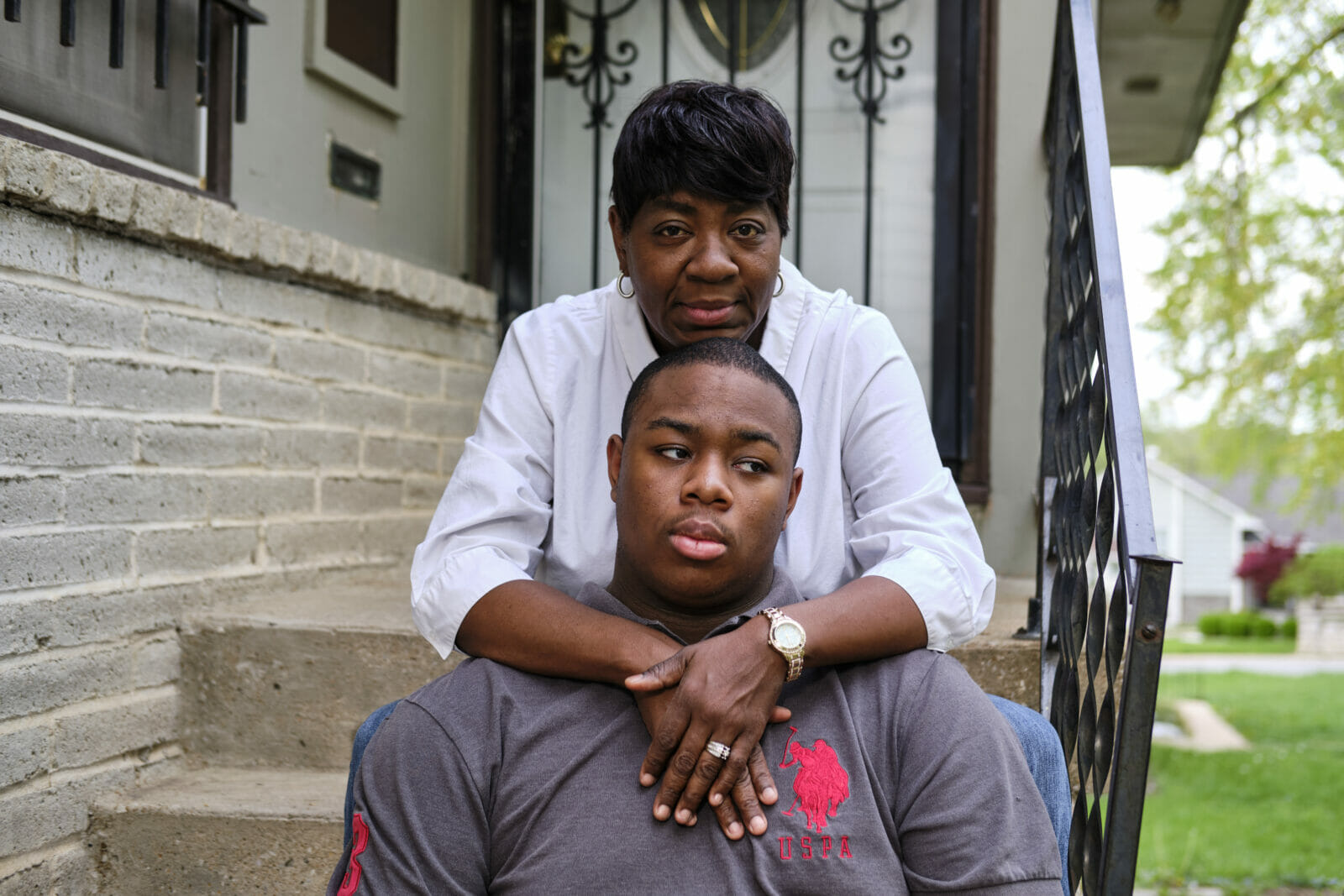 A Black mother with short hair and a white blouse crosses her arms around her 17-year old son who has autism. Michelle Mitchell worries about the small things in life, like sending Gerald to a bus stop. The bigger things, like career, are even more dizzying. (Dominick Williams | Flatland)