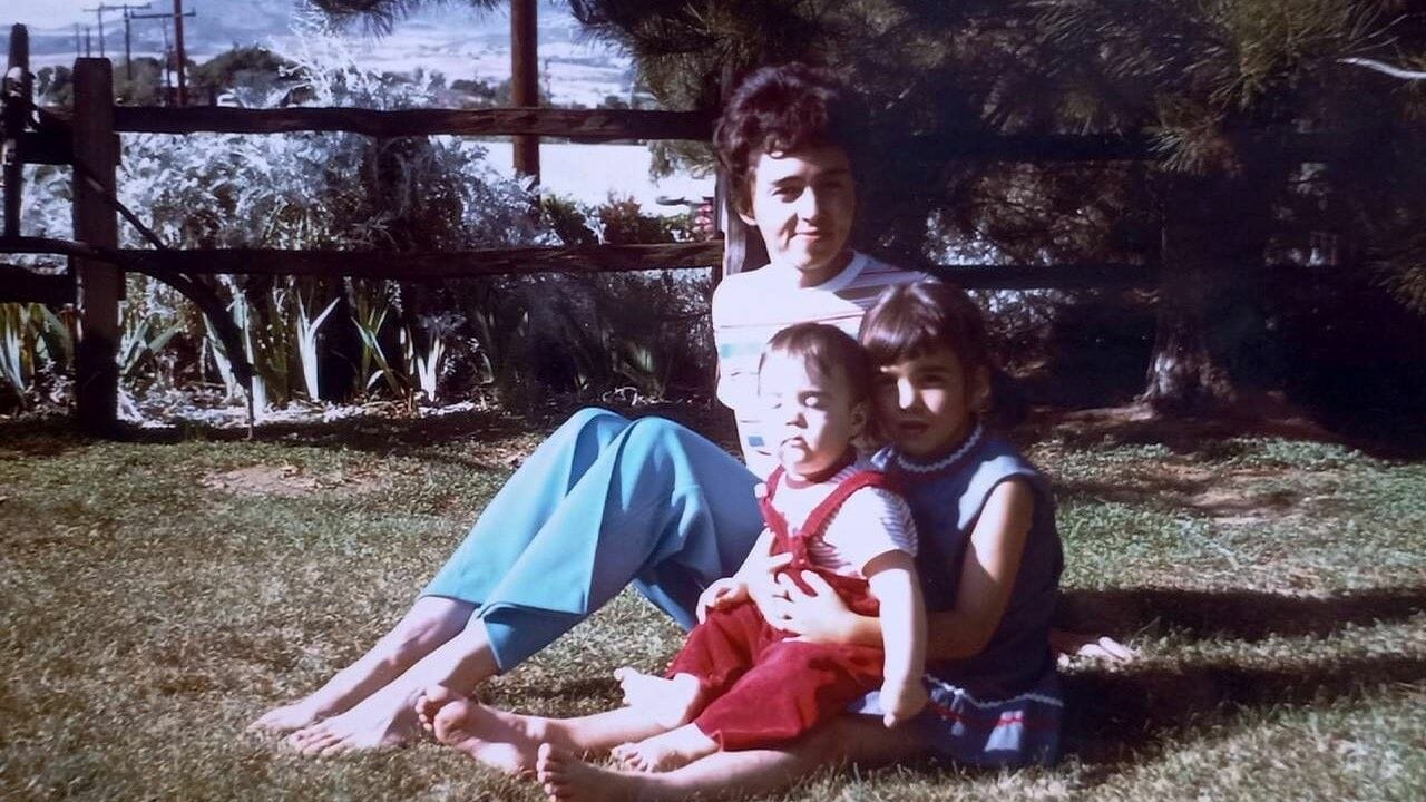 A mother and two children sitting in the grass.
