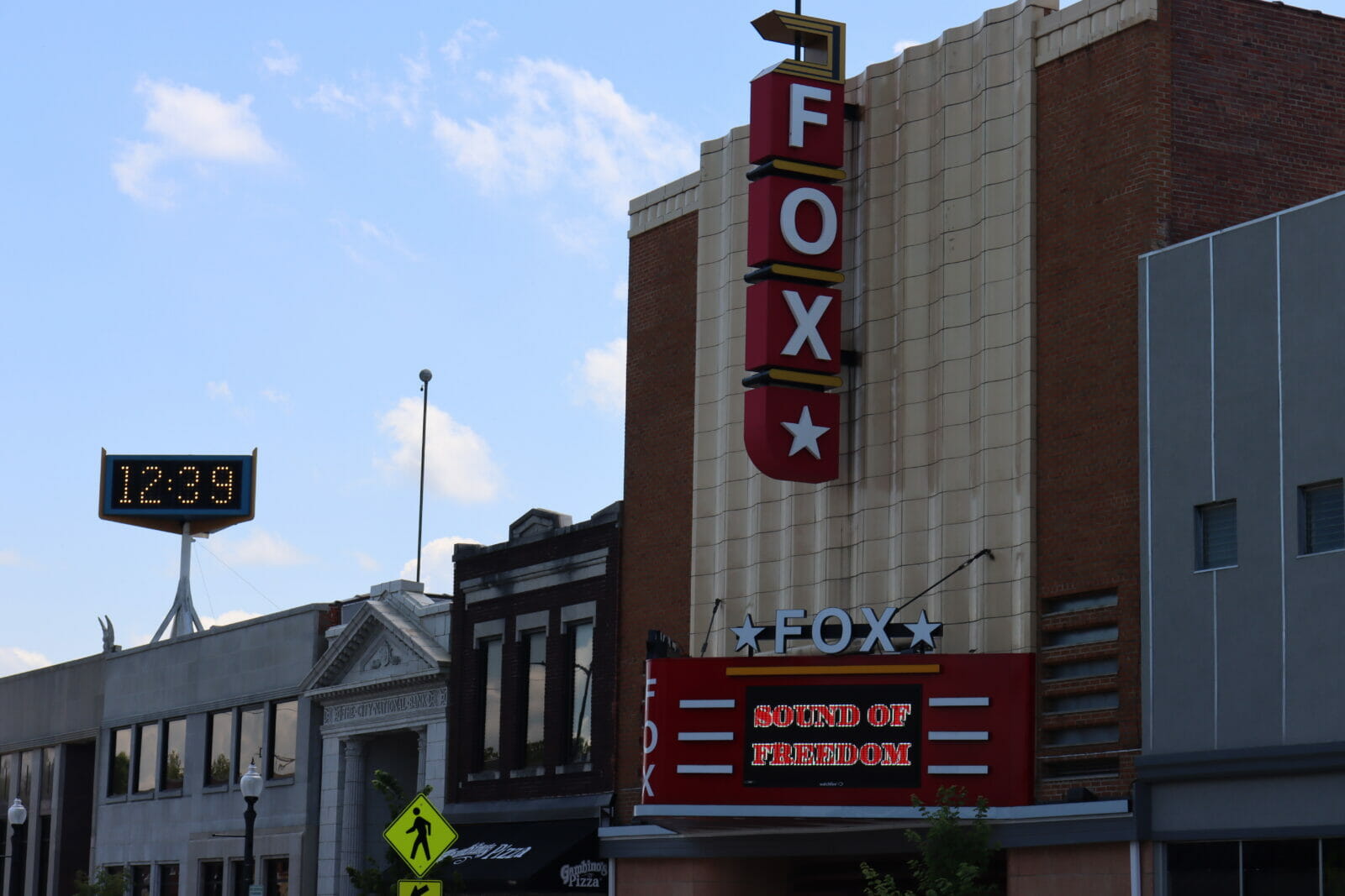 A vertical sign on a tall brick and white stone building reads "FOX" lower down a digital marquee reads "Sound of freedom"