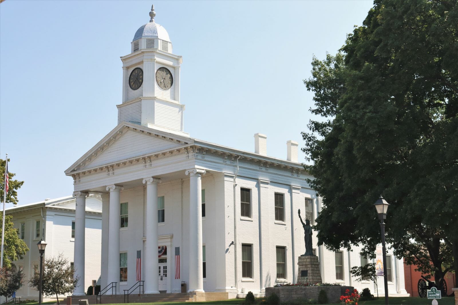A white courthouse built in the Greek revival style. On top the building is a clock tower.