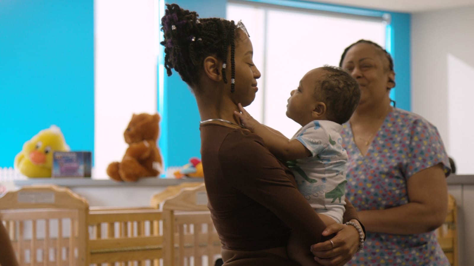 Woman holds young boy while older woman looks on in child care facility