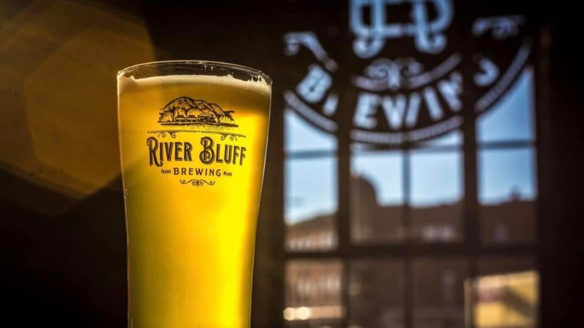 River Bluff Brewing beer in a glass in front of a window.
