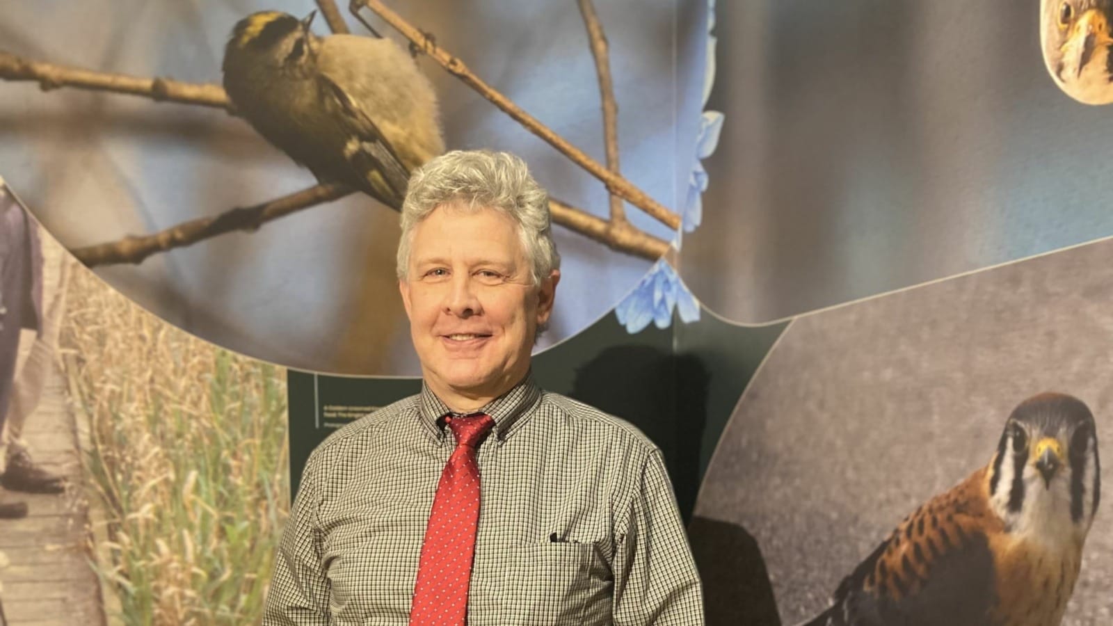 Eric Ward, vice president for public programming for Linda Hall Library, standing between two of his three photographs shown at the ornithology exhibition. Ward is particularly fond of the Brown-headed Nuthatch reintroduction display next to his pictures. He describes their distinct call as “sounding just like a rubber ducky.”